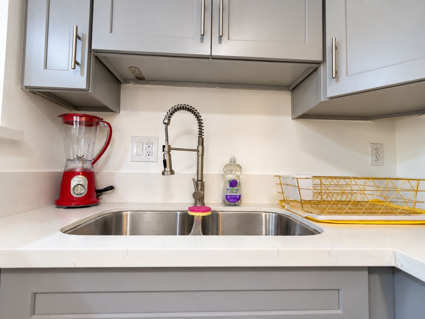 A kitchen with a stainless steel sink, a red blender, a faucet, and a soap dispenser.