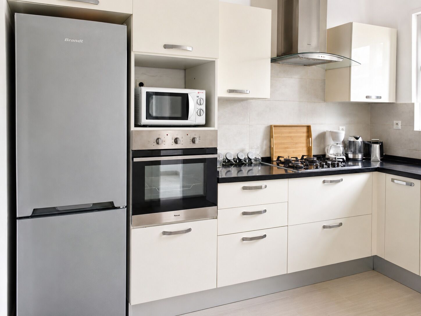 A modern kitchen with a Brandt refrigerator, a microwave, an oven, a gas stove, and white cabinetry.