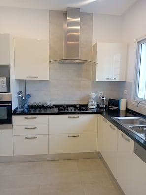 Una cocina moderna con armarios blancos, encimera negra, electrodomésticos de acero inoxidable y una ventana que proporciona luz natural.