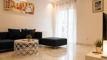 A modern living room with a sofa, ottoman, and coffee table, a painting on the wall, and a window with curtains.