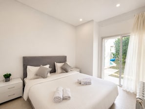 Un dormitorio moderno con una cama grande, una mesita de noche, una planta pequeña y vistas al exterior.