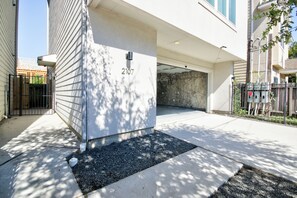 Ein Gebäudeeingang mit der Hausnummer 2107 an der Wand, einem Betonweg und einem Metallzaun.