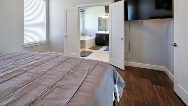 Ein Schlafzimmer mit einem großen Bett, ein Badezimmer mit Spiegel und Waschbecken sowie ein an der Wand befestigter Fernseher.