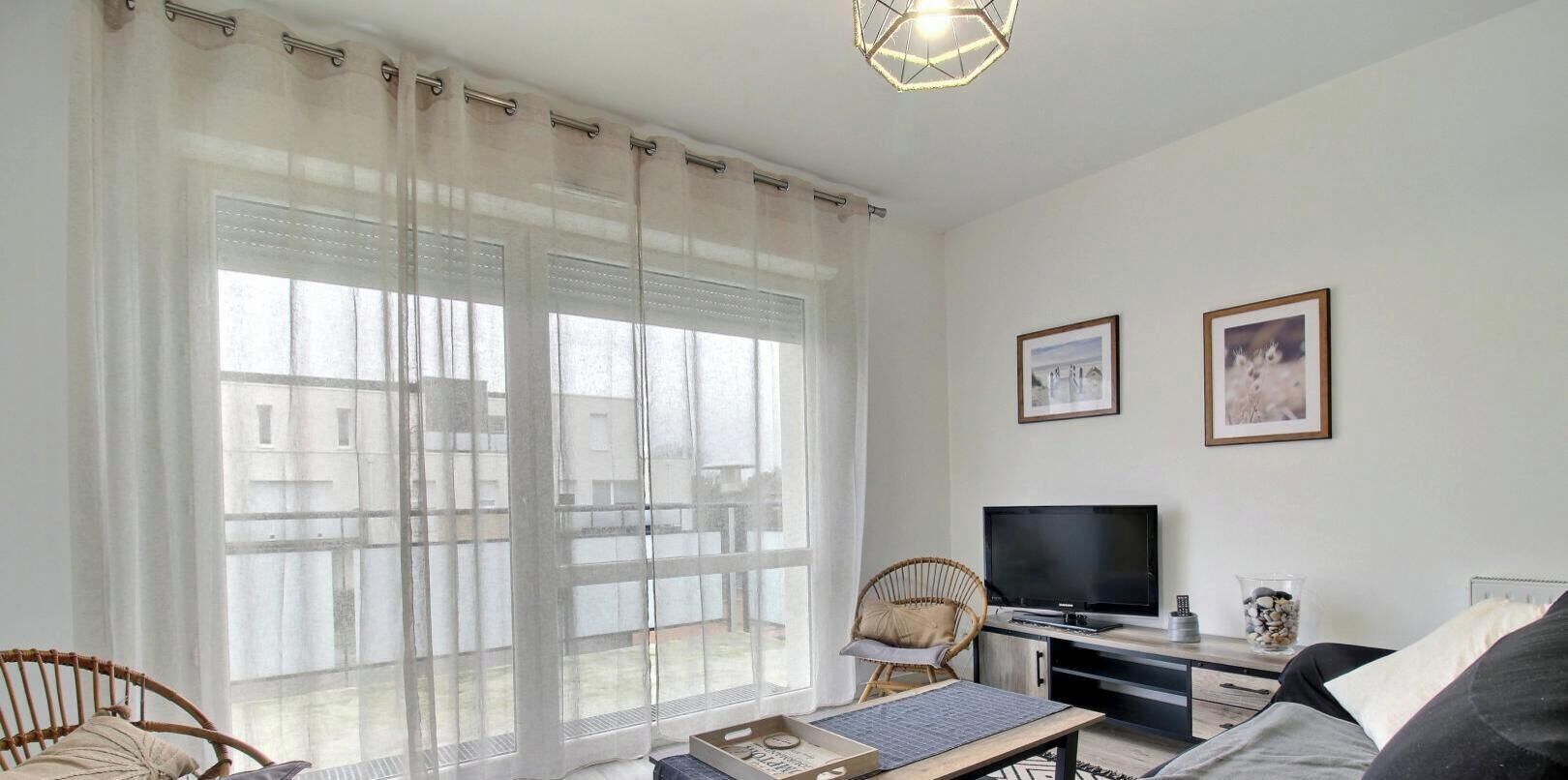 Een woonkamer met een groot raam, een televisie, een fauteuil en een bank.