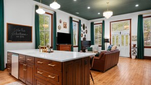 A spacious living room with a large wooden cabinet, a television, a sofa, and a chandelier. - Schoolhouse | Fenced Yard | Family & Dog Friendly (Traverse City)