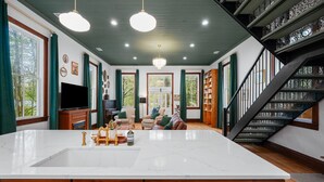 A spacious living area with a large marble island, a staircase, and a view of the outdoors. - Schoolhouse | Fenced Yard | Family & Dog Friendly (Traverse City)