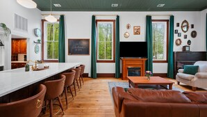 A spacious living room with a fireplace, a television, and a dining area with bar stools. - Schoolhouse | Fenced Yard | Family & Dog Friendly (Traverse City)