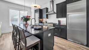 A modern kitchen with a central island, dark cabinetry, stainless steel appliances, and a pendant light. - 🦩Book Me Baby! Sun Of A Beach in Santa Rosa Beach~Golf Cart Included🦩 (Santa Rosa Beach)