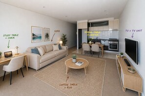 A modern living room with a study table, sofa, coffee table, rug, dining table, TV unit, and kitchen area. - Stylish Sydney·2BR·UNSW, Beach, Parking, Sleeps 6 (Kingsford)