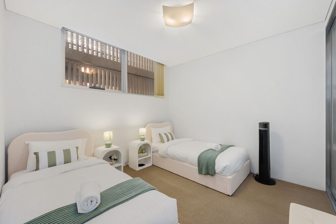 Een hotelkamer met twee bedden, nachtkastjes met lampen, een groot raam met jaloezieën en een staande verwarming.