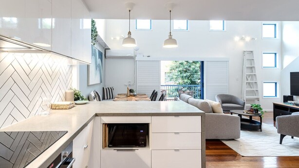 A modern kitchen with a built-in oven, a dining area with a sofa, and a view of the outdoors. - Biggera Breeze Retreat (Biggera Waters)
