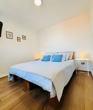 Ein Schlafzimmer mit einem Bett, Holzboden, weißen Wänden und einem Nachttisch mit Lampe.