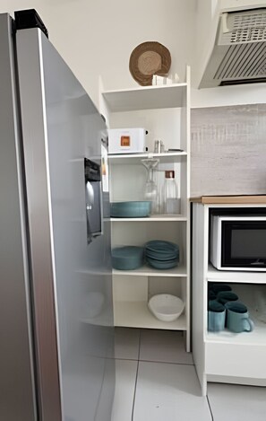 Eine Küche mit Kühlschrank, Mikrowelle und Regalen mit Geschirr und Behältern.