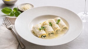 A plate of rolled pasta with a creamy sauce, garnished with basil, on a white plate. - Mio Trancoso (Porto Seguro)