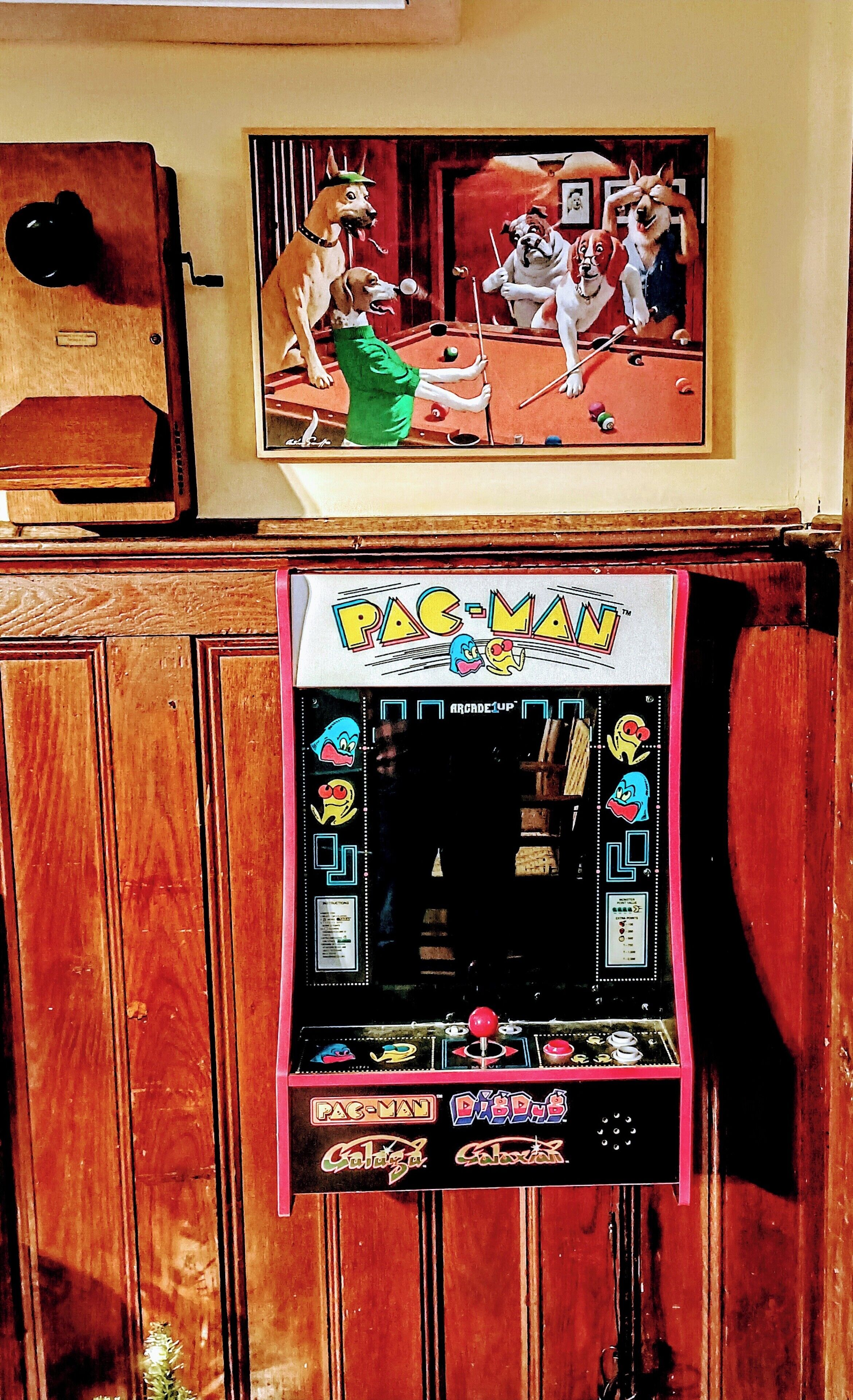 A Pac-Man arcade machine with a wooden cabinet, a framed Pac-Man poster, and a vintage jukebox.