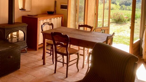 Uma sala de jantar com uma mesa e cadeiras de madeira, fogão e vista para o exterior.