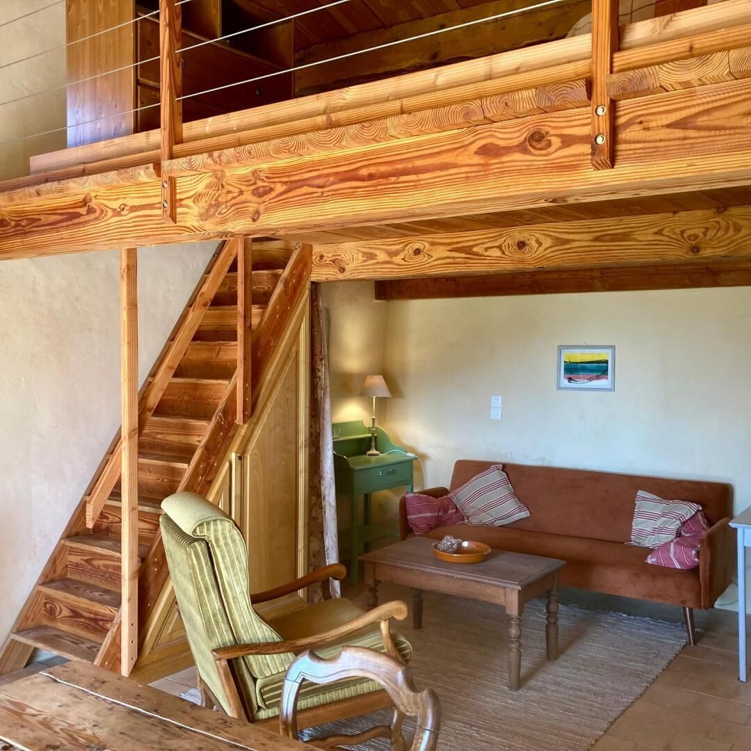 A wooden staircase leading to an upper level, a green upholstered chair, a brown sofa with striped pillows, and a small table with a lamp.