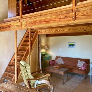 A wooden staircase leading to an upper level, a green upholstered chair, a brown sofa with striped pillows, and a small table with a lamp. - The Encantade Guesthouse (TREVILLACH)