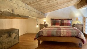 Quarto com teto de madeira, uma cama com colcha xadrez, duas mesas de cabeceira com abajures e uma cômoda de madeira.