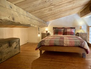 A bedroom with a wooden ceiling, a bed with a plaid bedspread, two bedside tables with lamps, and a wooden chest of drawers. - The Encantade Guesthouse (TREVILLACH)