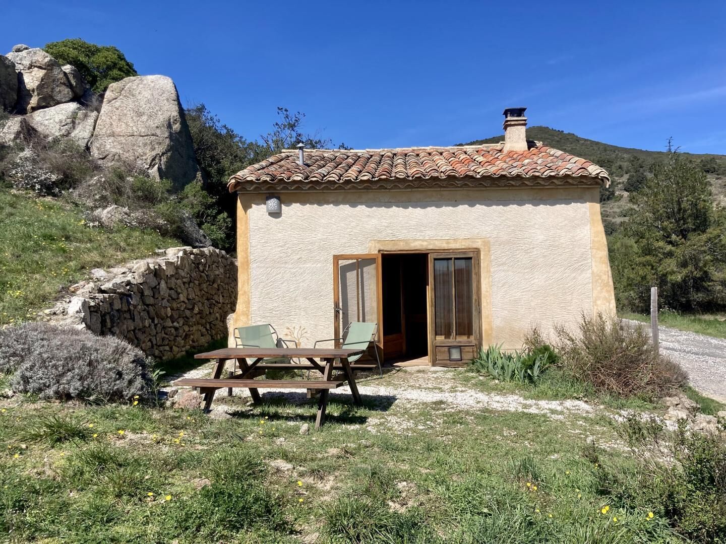 Un petit edifici de pedra amb teulada d'argila, una porta de fusta i una taula amb caires a l'exterior.