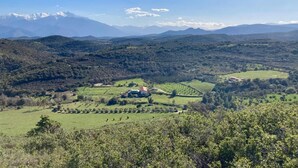 Paisagem rural com uma casa cercada por campos e montanhas ao longe.