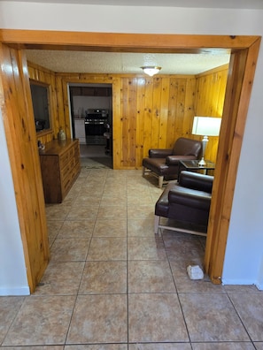 Ein Wohnzimmer mit Holzboden, einem braunen Ledersofa, einer Holzkommode und einer Küche im Hintergrund.