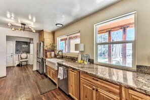 A kitchen with wooden cabinets, granite countertops, a stainless steel refrigerator, and a large window with a view of the outdoors.