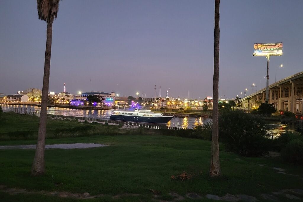Vista al agua con un barco amarrado, un edificio iluminado al fondo y un cartel.