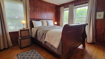 A wooden-paneled bedroom with a bed, bedside lamps, a window with curtains, and a small rug.