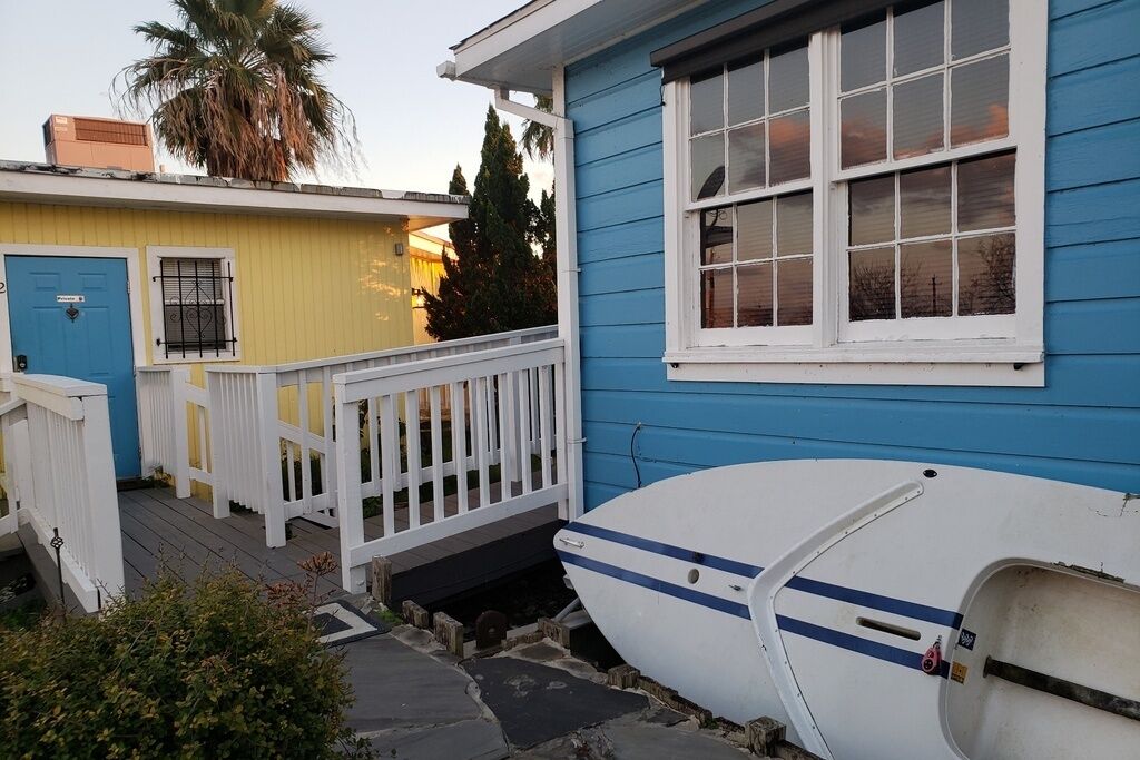 Une maison à l’extérieur bleue, avec un porche blanc et un bateau devant.