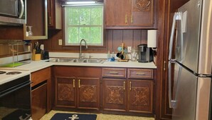 Una cocina con armarios de madera, un refrigerador de acero inoxidable, un microondas y una ventana con persianas.