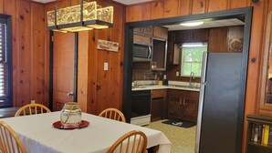 Un comedor con una mesa, sillas y un adorno decorativo. Junto a él, una cocina con electrodomésticos y armarios.
