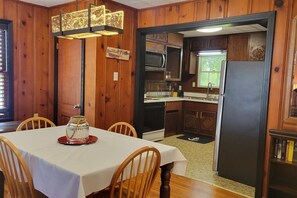 Zona pranzo con tavolo, sedie e un elemento decorativo al centro. Accanto, una cucina completa di elettrodomestici e mobili.