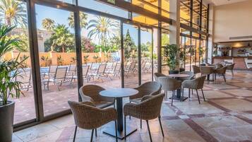 A hotel lobby with a pool view, wicker chairs, and a bar area.