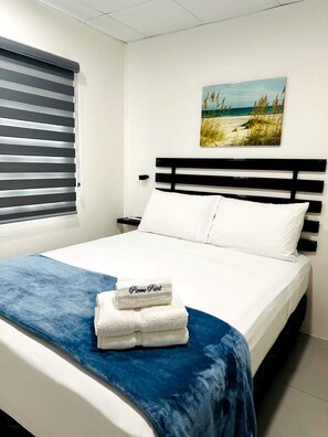 A bed with a white and blue bedspread, a headboard, and a painting of a beach scene on the wall.