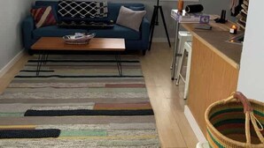 Een woonkamer met een bank, salontafel en een keukenhoek met een aanrecht en krukken.