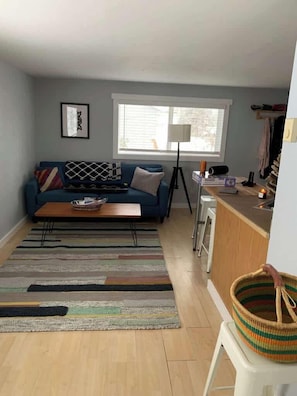 A living room with a sofa, coffee table, and a kitchen area with a counter and stools. - Upper Pine Vacation Rental | Bend Living (Bend)