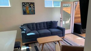 Een woonkamer met een donkerblauwe bank, een houten salontafel en een kleurrijk gestreept vloerkleed.