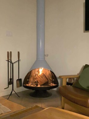 A room with a wood-burning stove, a chair, and a small table. - Lower Pine Vacation Rental | Bend Living (Bend)
