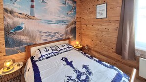 Een kamer met een bed, een schilderij van een strand, een vuurtoren en een klein tafeltje met een lamp.