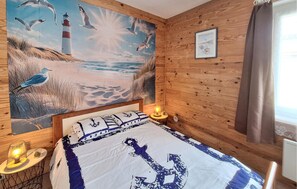A room with a bed, a painting of a beach scene, a lighthouse, and a small table with a lamp. - 2 bedroom amazing home in Soulac-Sur-Mer (Soulac-Sur-Mer)