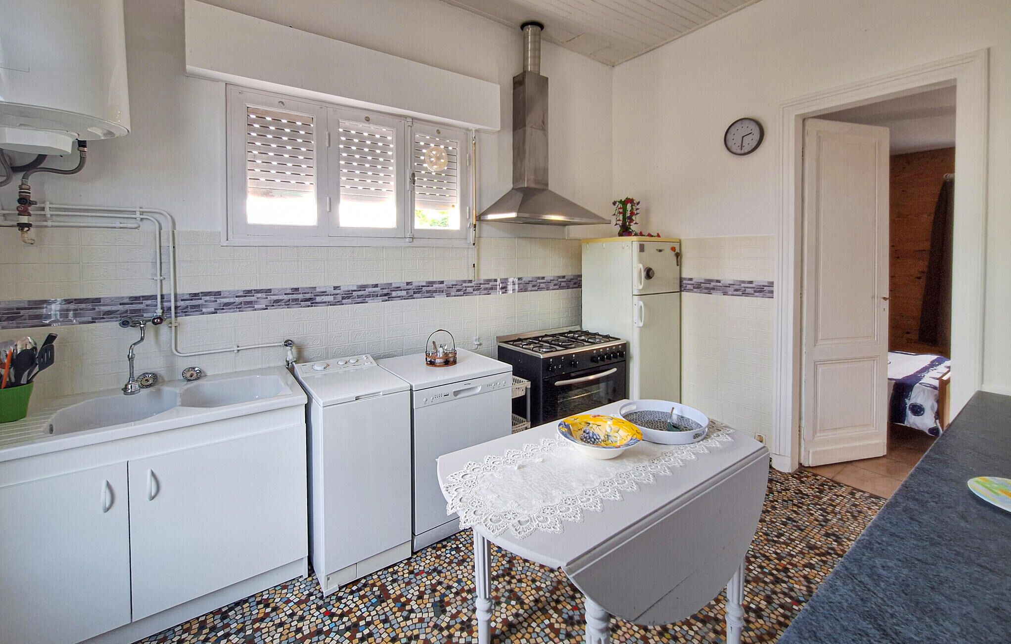 A compact kitchen with a sink, stove, and refrigerator, featuring a tiled backsplash and a small table with a lace tablecloth.