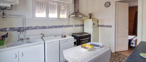 A compact kitchen with a sink, stove, and refrigerator, featuring a tiled backsplash and a small table with a lace tablecloth.