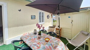 Een terras met een tafel, stoelen, een grote parasol en een bloempot.