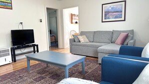 Ein Wohnzimmer mit Fernseher, Sofa und blauem Sessel.
