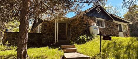 A stone house with a porch, a gas cylinder, and a sign reading 'Saker.'