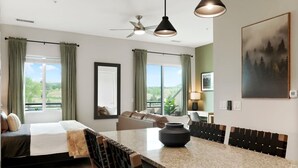 Una camera d'albergo moderna con un letto, zona salotto, angolo ristoro, ampie finestre e opere d'arte.