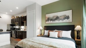 Una camera d'albergo moderna con un letto, lampade da comodino, un quadro, un angolo cottura e vista sulla città.