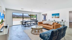A spacious living room with a large window, a round coffee table, a sofa, and a dining area.